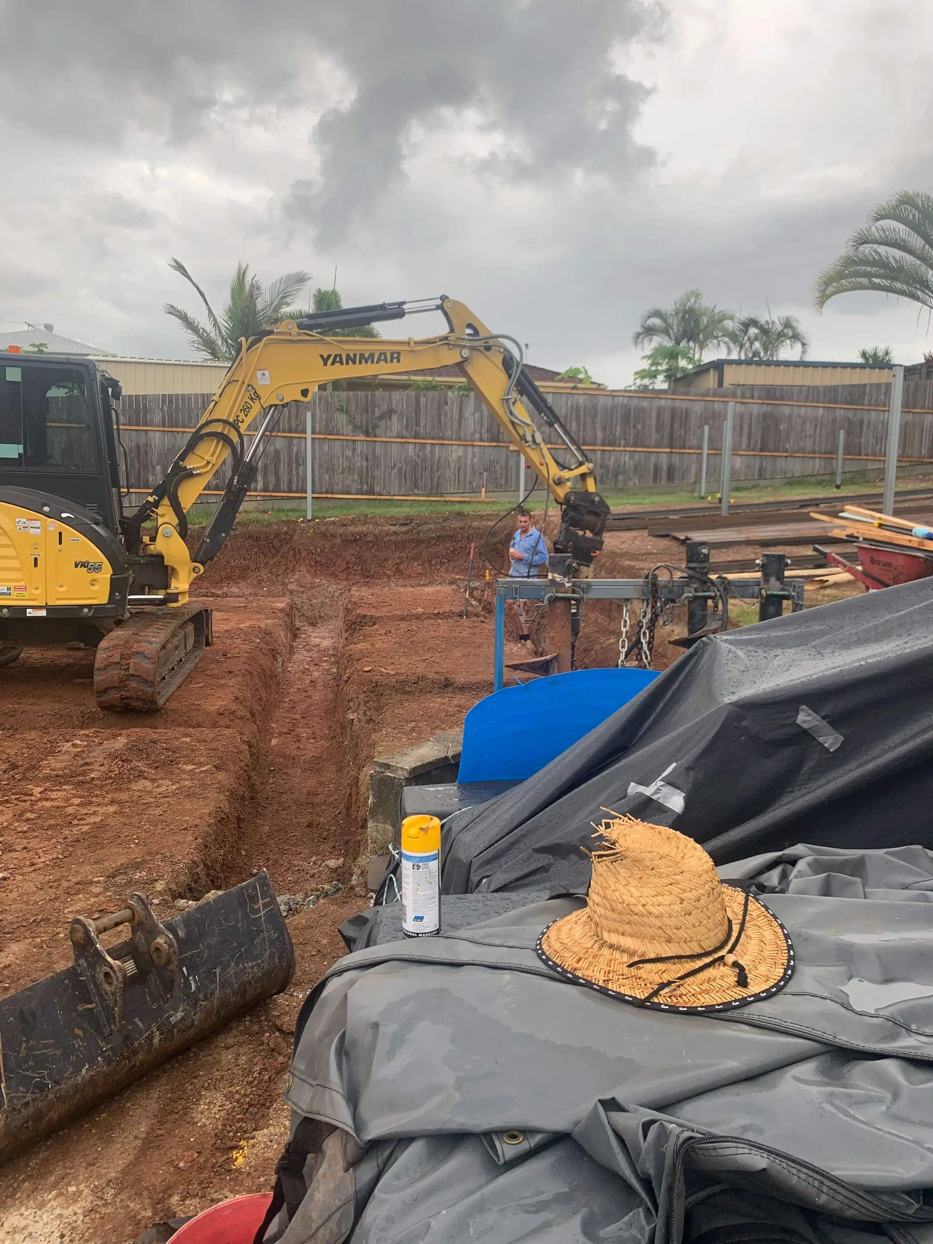 Yanmar excavator digging a service trench on a Brisbane site under storm cloud