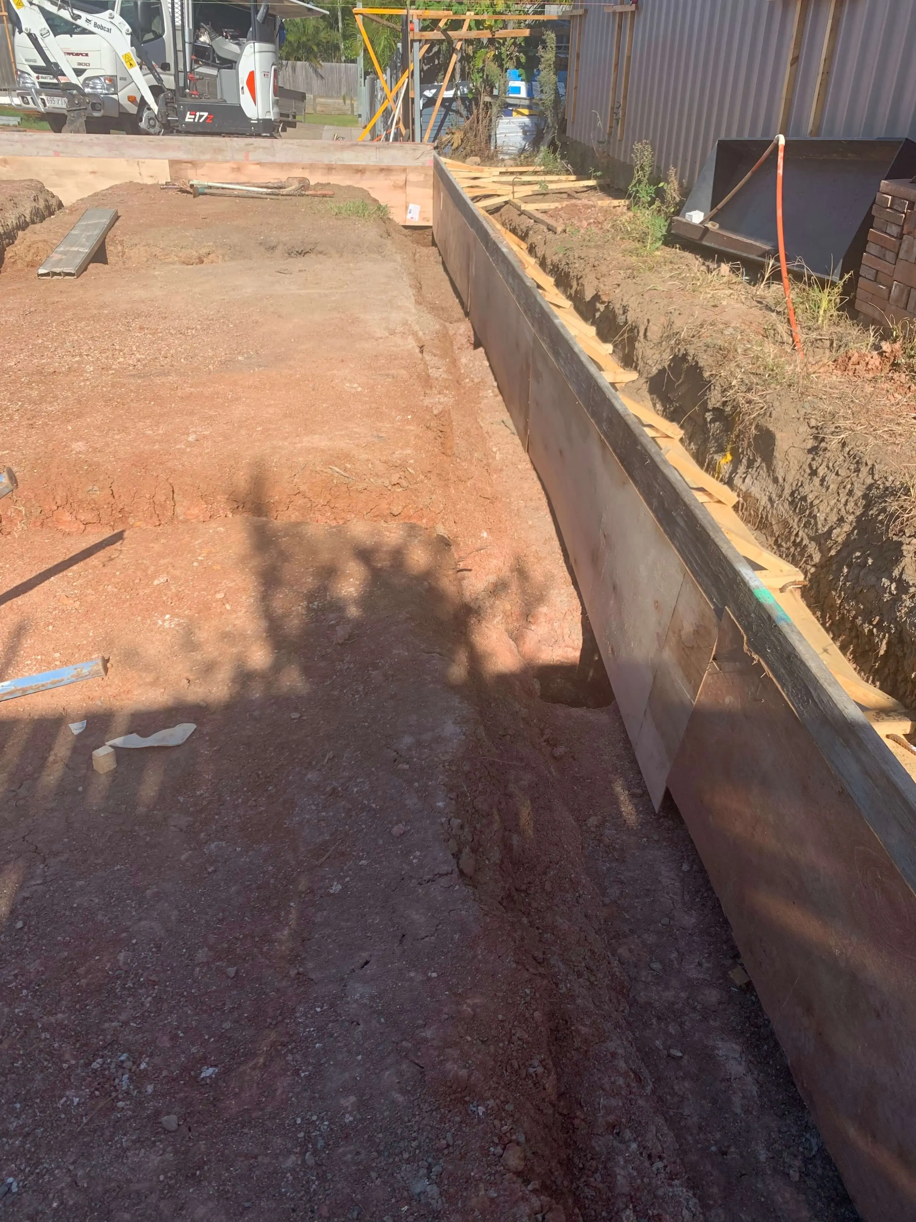 Formed footing trench with steel edge boards beside a Bobcat mini excavator