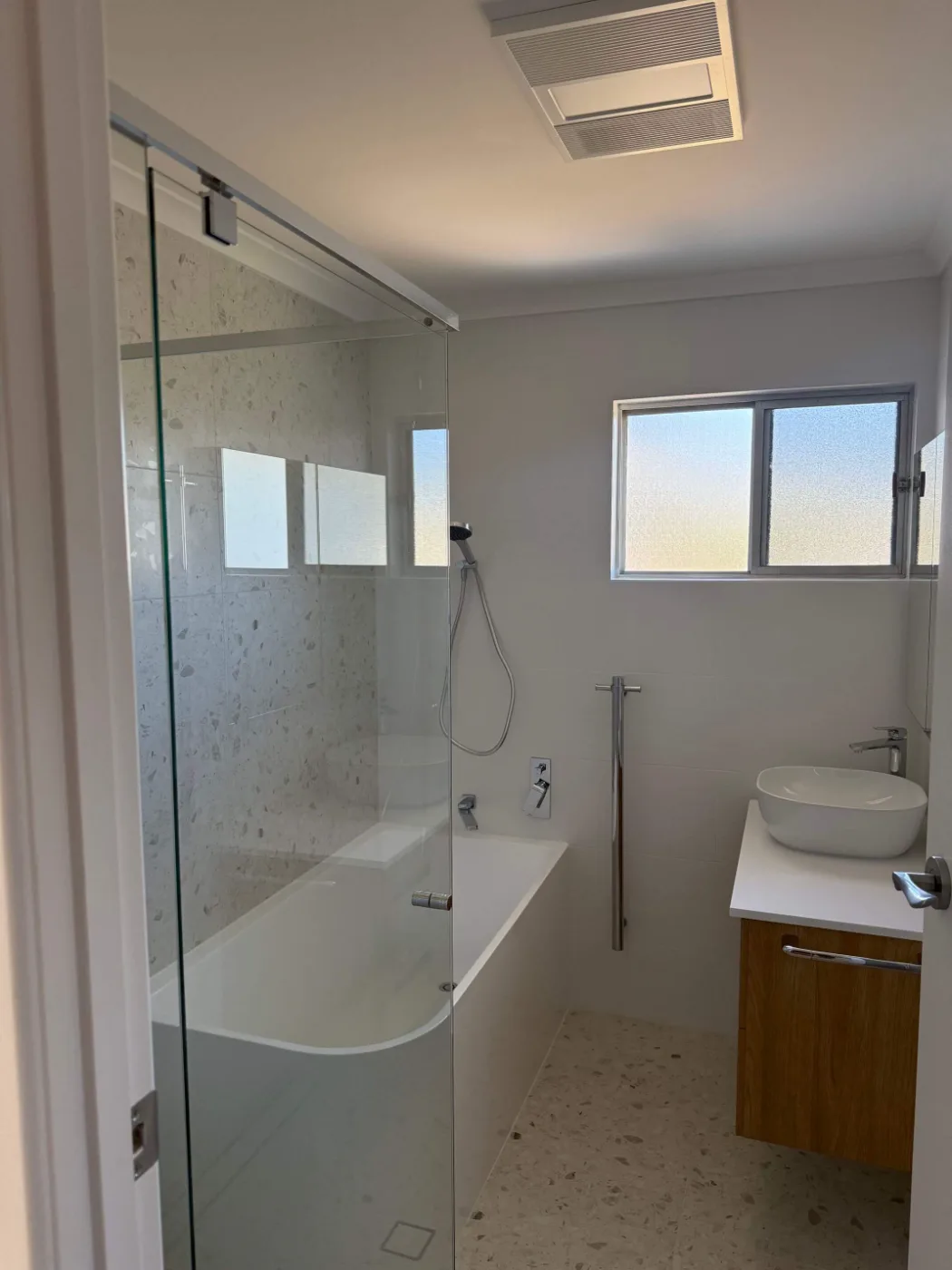 Frameless shower screen over a bath in a completed Brisbane bathroom renovation