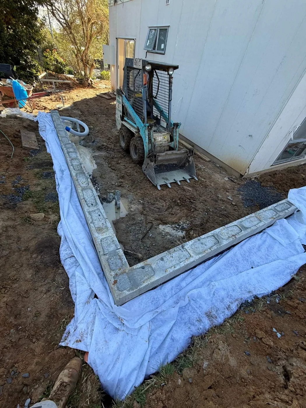 Skid steer excavating footings for a retaining wall beside a Brisbane home renovation