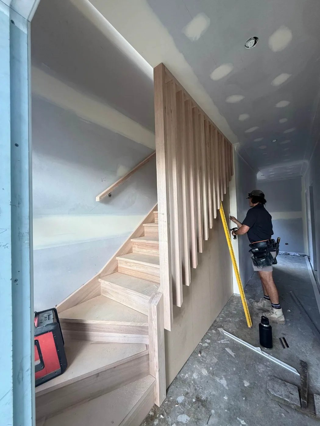 Carpenter installing a timber slat feature wall beside a new staircase, Brisbane renovation