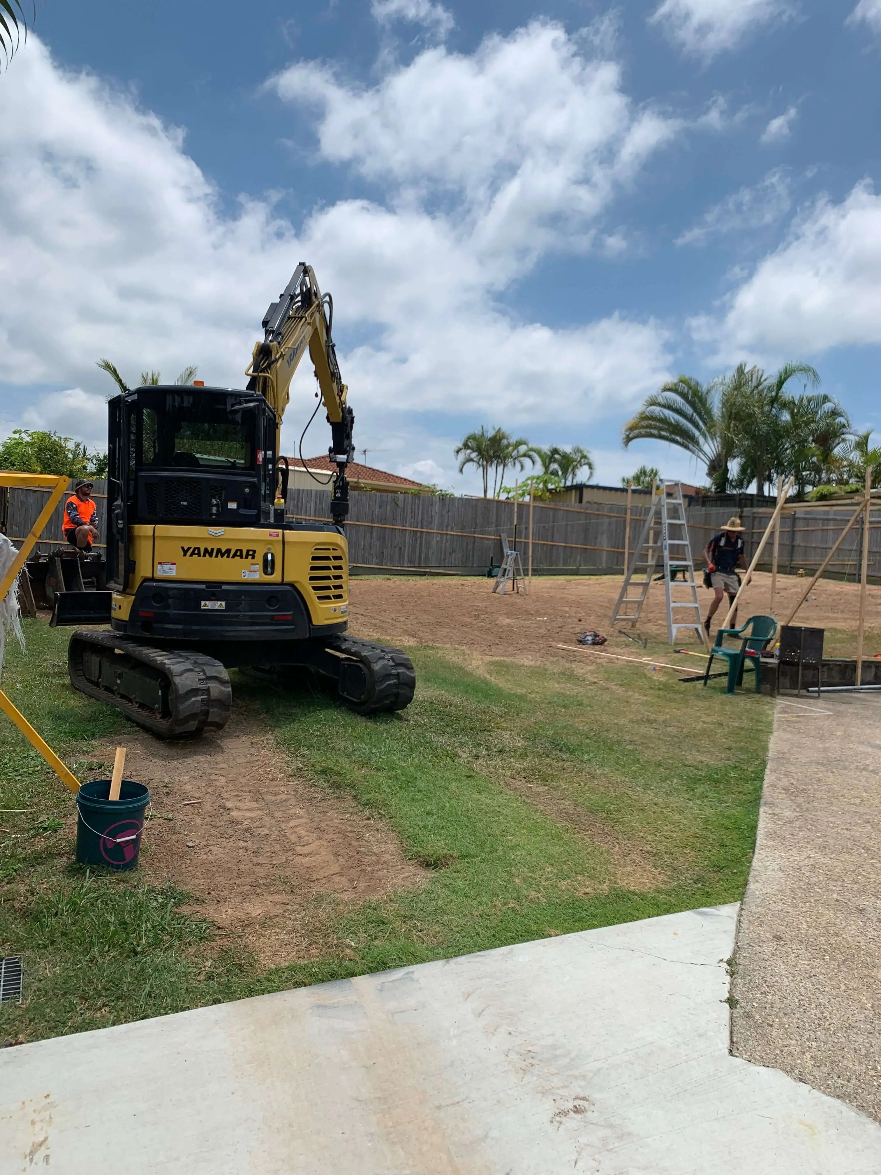 Yanmar excavator parked on a backyard pad beside setout profiles and ladders